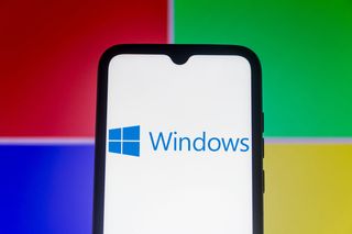 Windows logo appearing on a smartphone set against a bright Windows logo taking up the entire background