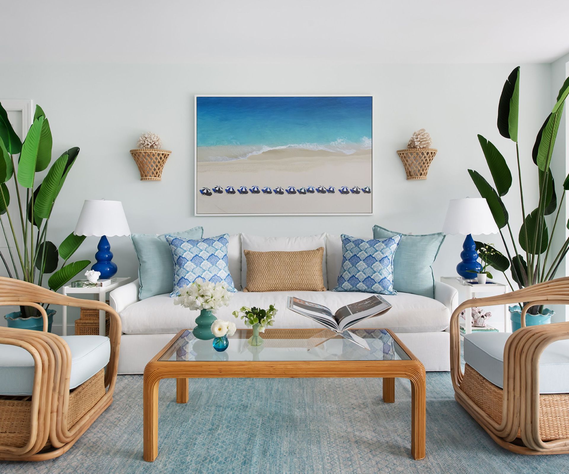 Nautical living room with blue carpet, white rattan armchairs, white sofa with blue pillows and large plants