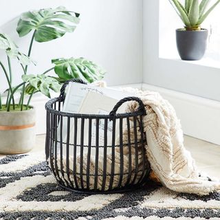 Dunelm Wicker Black Storage Basket containing blanket on a black and white floor rug