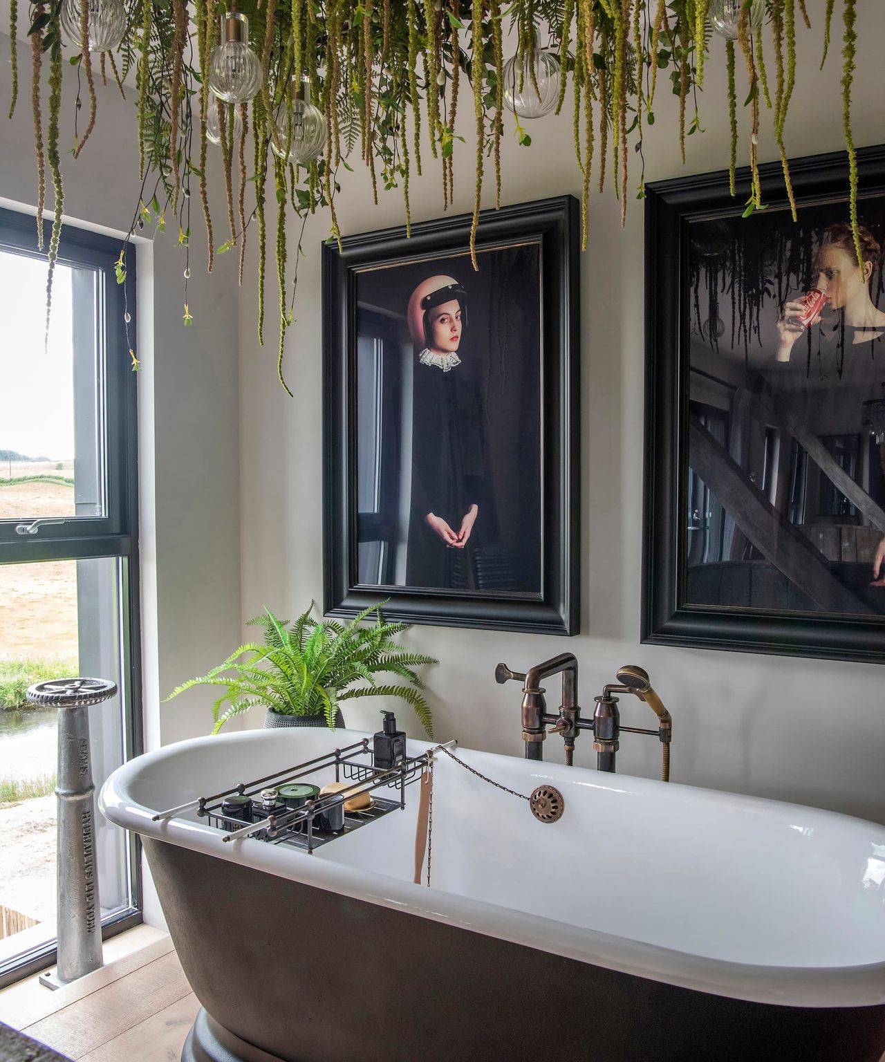 A bath with plant lighting above and two hanging portraits