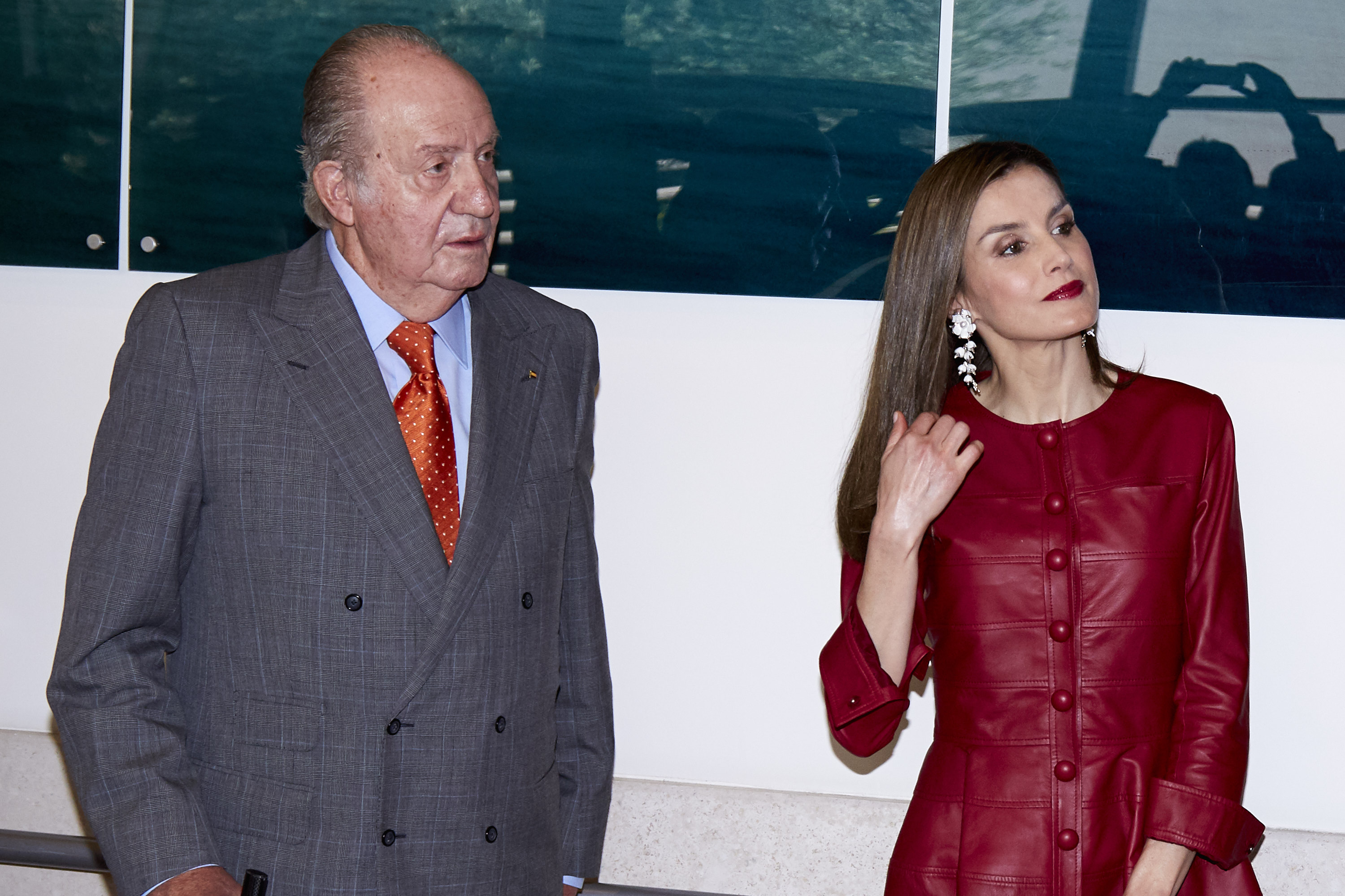 King Juan Carlos in a gray suit, standing next to Queen Letizia wearing a red coat