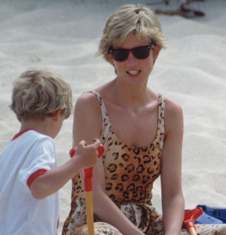 Princess Diana in a leopard print bathing suit sitting on a beach with Prince William and another child