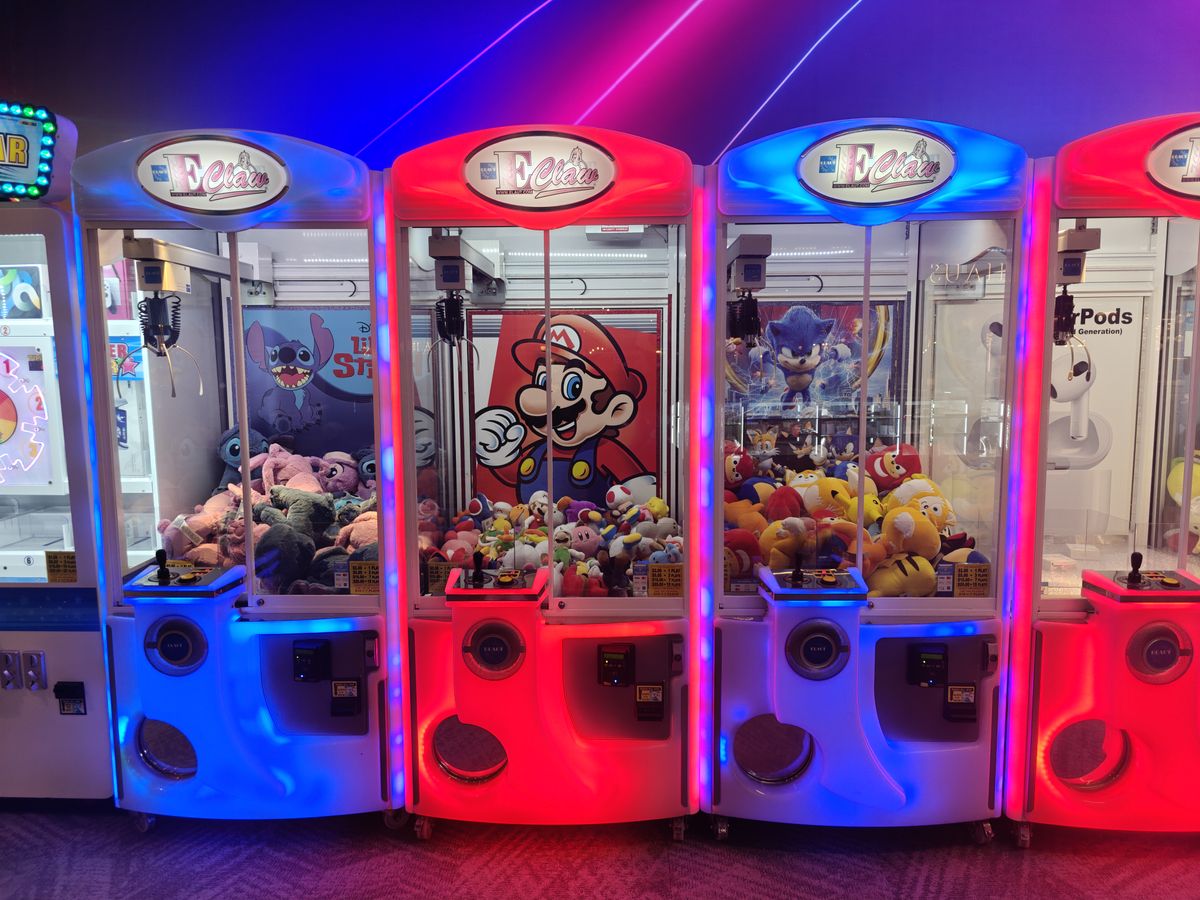 Una l&iacute;nea de juegos de gancho, con luces de ne&oacute;n y premios de peluche de Mario y Sonic en su interior