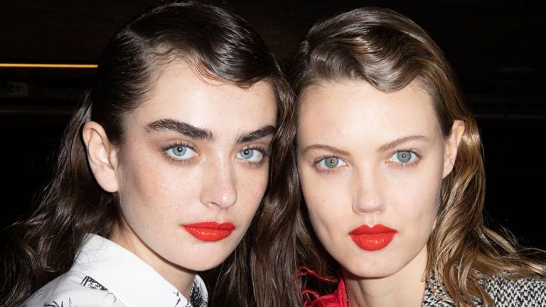 Two models with full brows wearing bright red lipstick