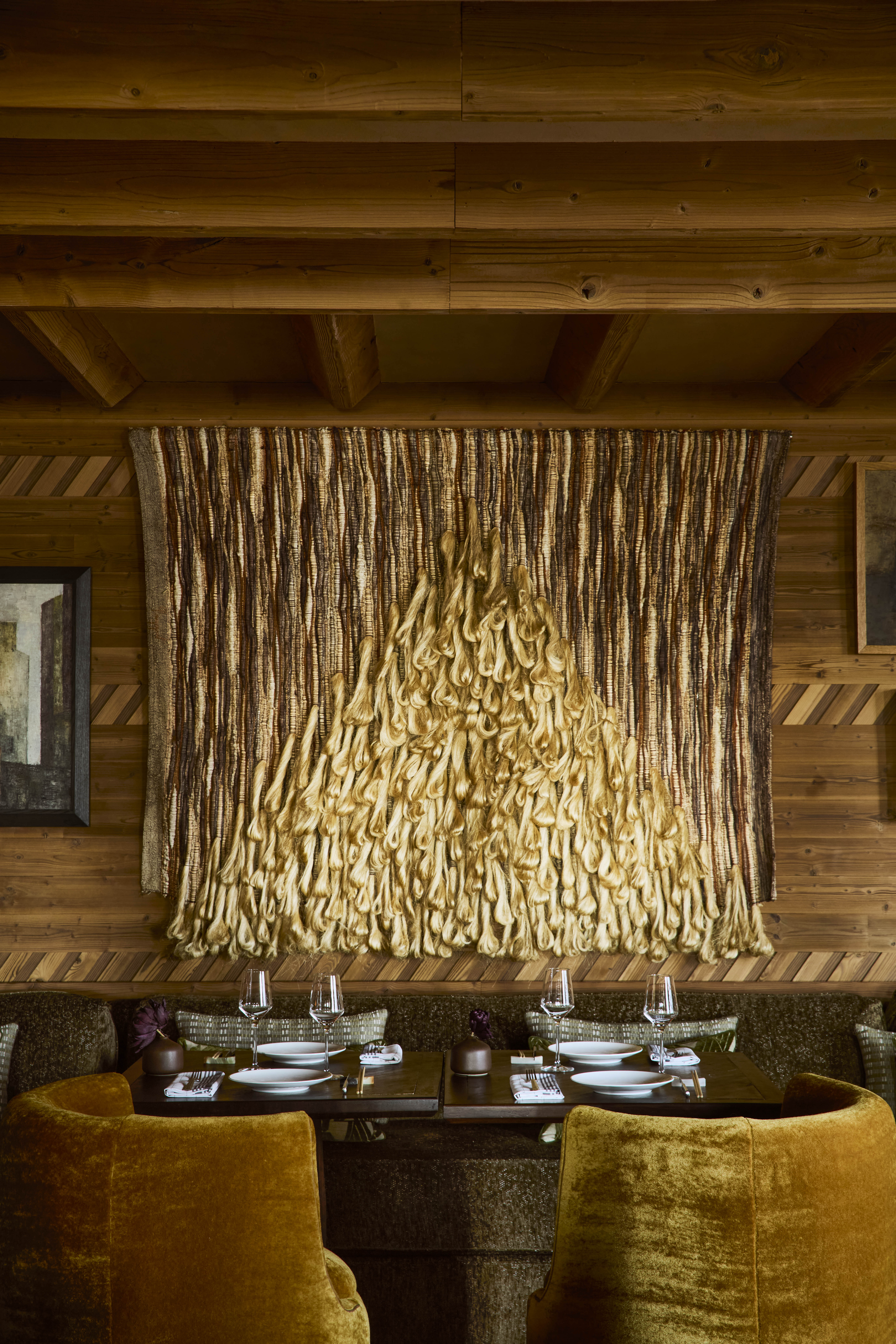 The elaborate, theatrical interiors of a ski chalet with wood wall paneling, plush textiles in different patternes, colors, and textures, plenty of paintings and sculptures adorning its halls, and a dimly lit atmosphere.