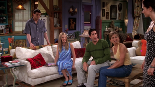 En bild från HBO Max-serien Vänner, där hela gänget är samlade runt soffan i vardagsrummet och tittar undrande på Monica.