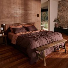 Dark red and orange bedding on a king size bed against a bare wall