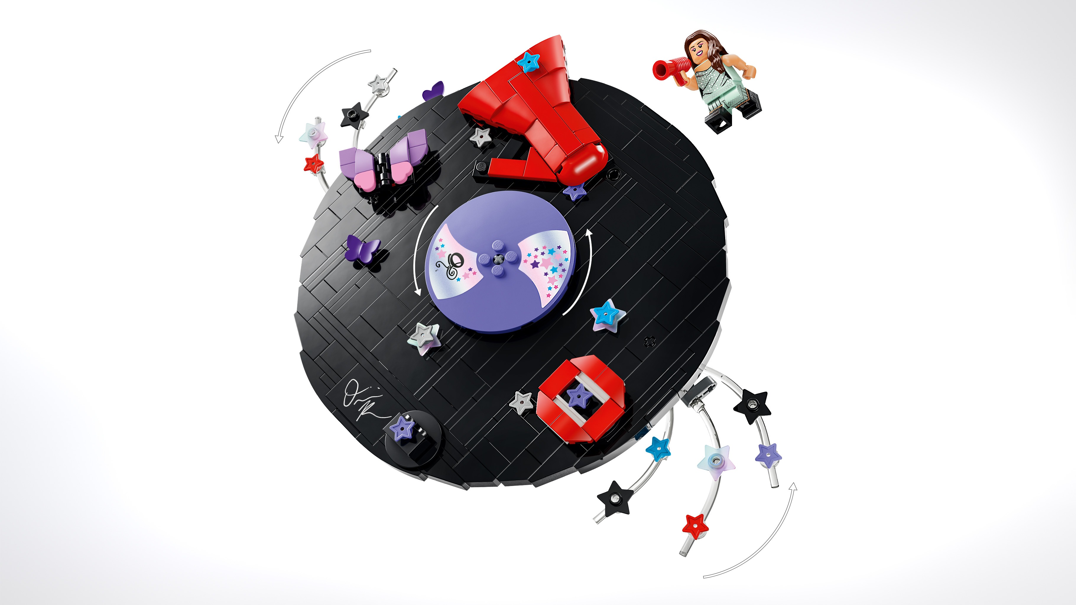 Overhead product shot of the Lego Vinyl set's circular black base, decorated with a megaphone, butterflies, stars and a purple centre disc, with a minifigure floating beside it against a white background.