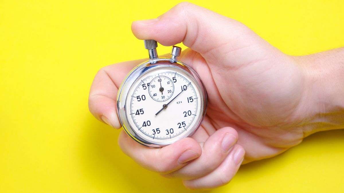 A hand holding a mechanical stopwatch on a yellow background