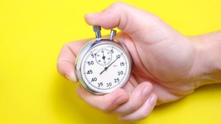 A hand holding a mechanical stopwatch on a yellow background