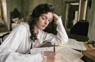 Anne Hathaway wears a nightgown while writing at a desk in 'Becoming Jane'