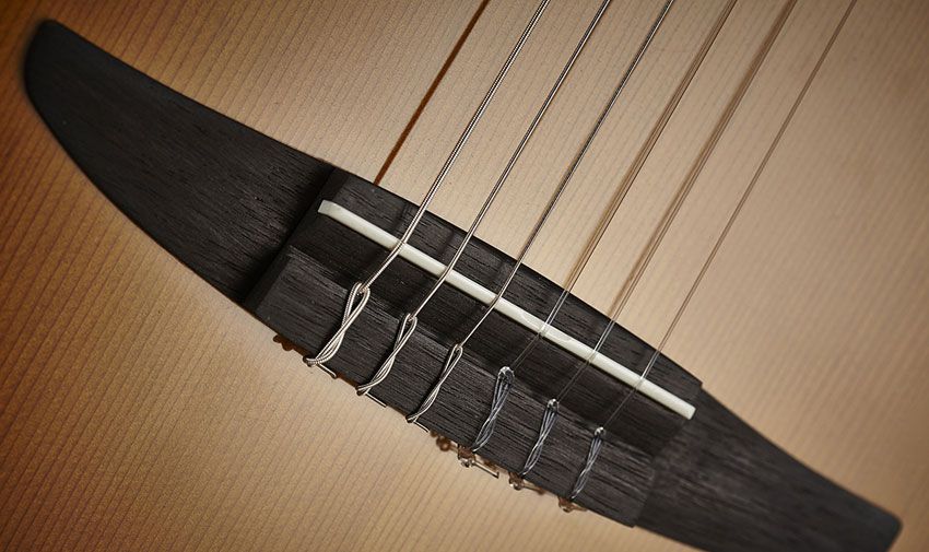 The guitar features a thin, wide classical-style rosewood bridge