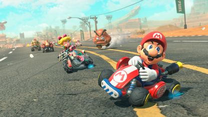Mario Kart World screenshot showing Mario drifting into pole position on a highway corner with Peach, Donkey Kong, Bowser, and Toad behind him, all while a giant goomba rushes the pack on foot