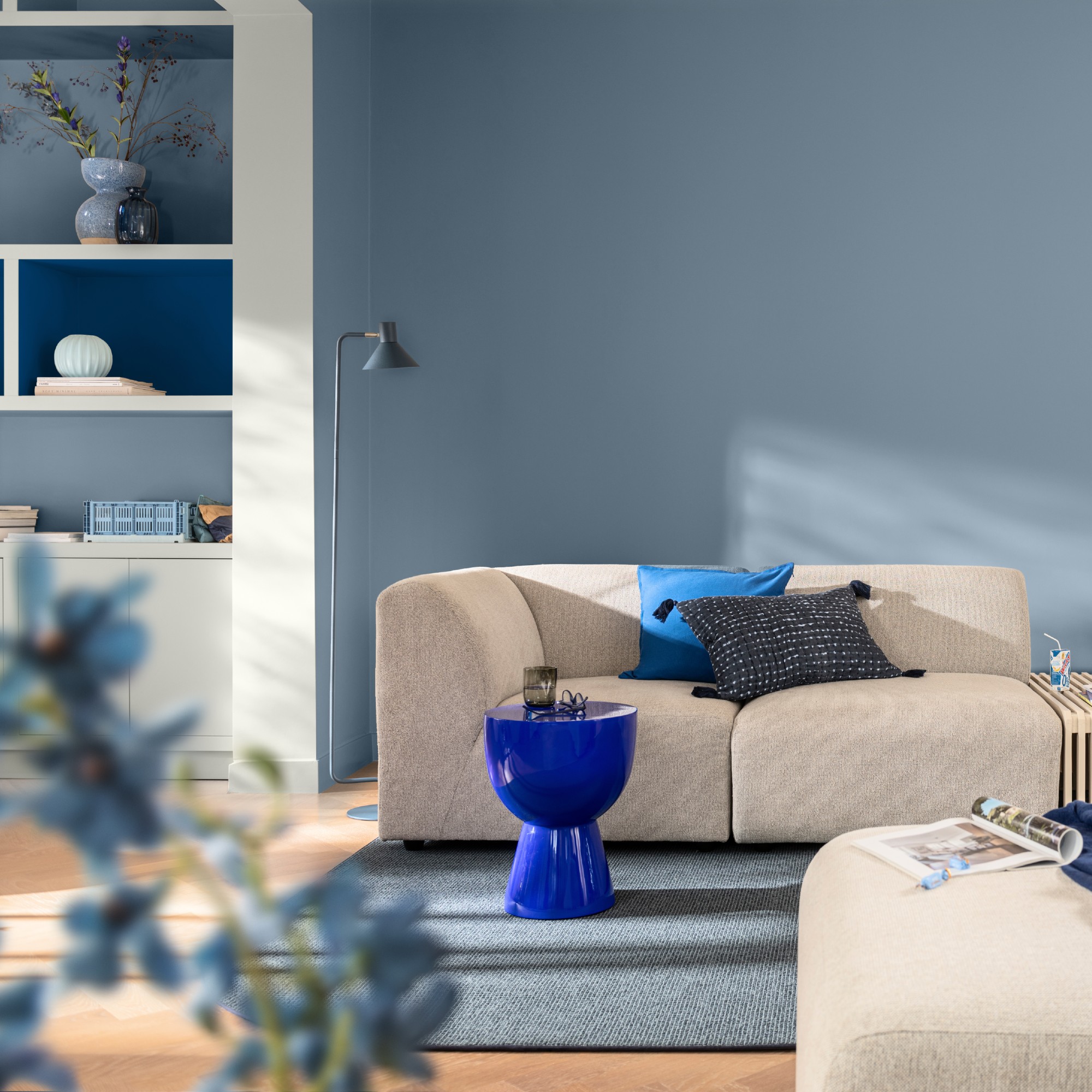 A living room painted in Dulux&#039;s Mellow Flow blue shade with an off-white modular sofa and open shelving painted in Mellow Flow and Free Groove