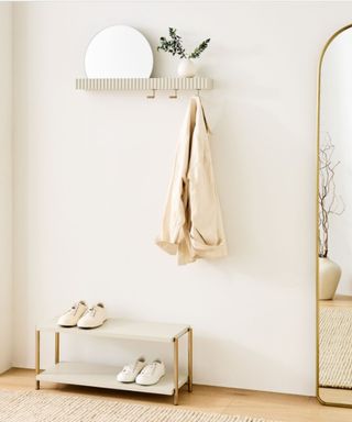 A white entryway with shoe storage, a tall gold arched mirror and a shelf with a small mirror