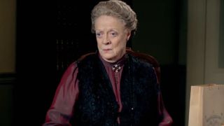 Dame Maggie Smith sitting in a chair during a conversation in Downton Abbey.