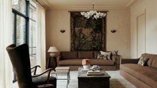 traditional style living room with limewash beige walls, brown slipcover sofas, large coffee table, two woven stools, armchair, tapestry, chandelier, and decorative plasterwork cornices