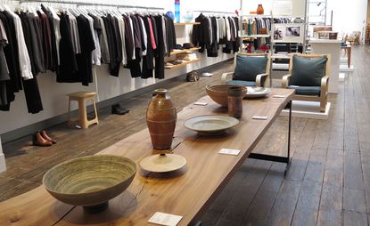Clothes on racks and wooden table with bowl and vase sculptures