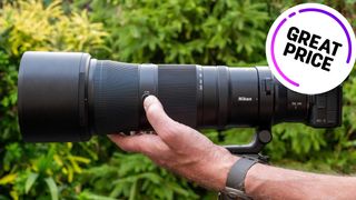 A hand holding the Nikon Z 180-600mm lens with a great price deal logo