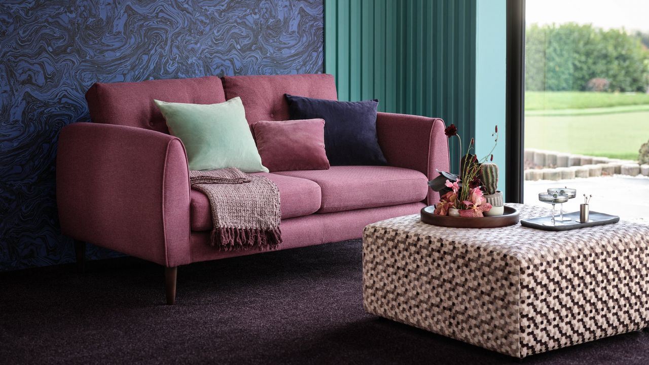 carpet colour trends for 2023, living room with aubergine carpet, check footstool, pink sofa, blue marble style wall, view to garden 