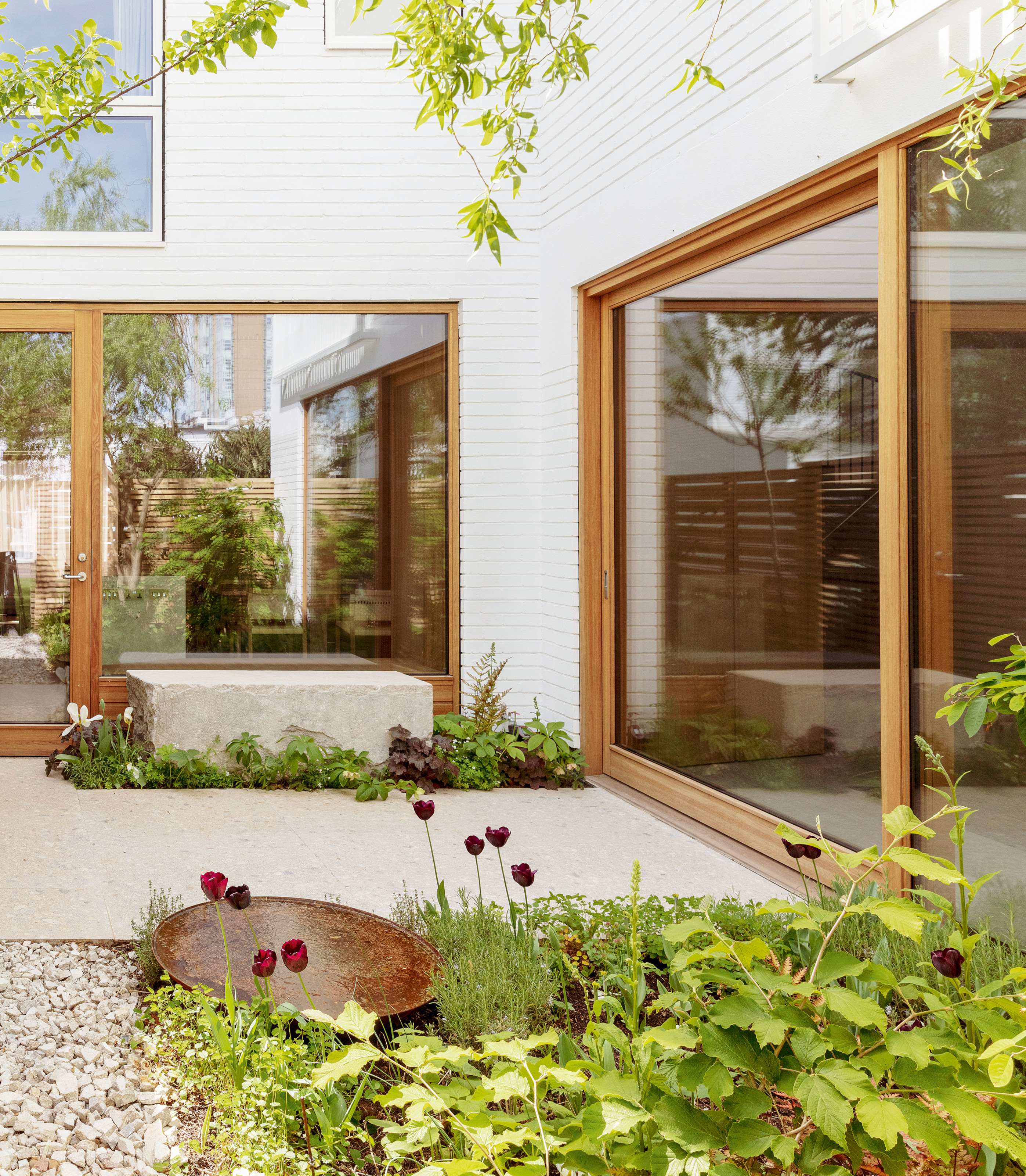 White stone patio with white stone bench against a full-height window surrounded by greenery