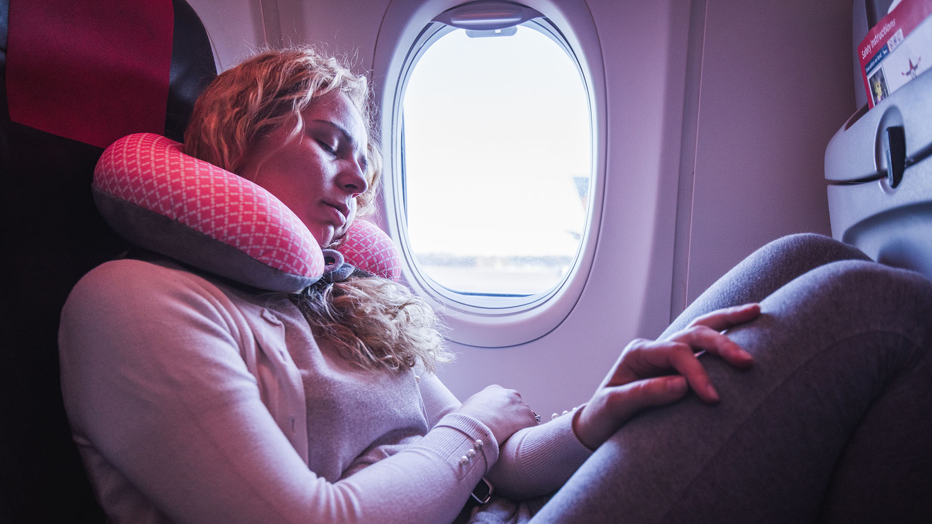 Woman asleep on a plane, using a travel pillow