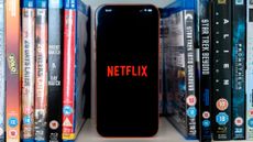 Netflix logo on an iPhone 17 Pro Max stood amongst Blu-rays