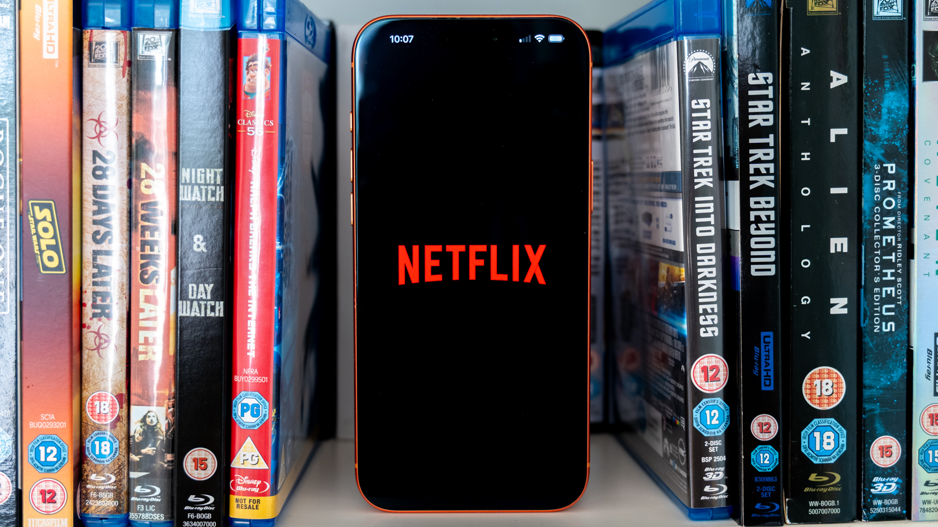 Netflix logo on an iPhone 17 Pro Max stood amongst Blu-rays