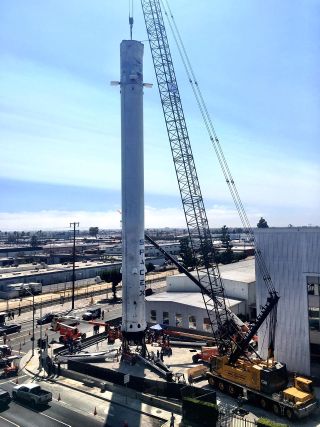 A crane positions the 15-story-tall Falcon 9 first stage before workers reattached its four deployable landing legs at SpaceX’s headquarters in Hawthorne, California.
