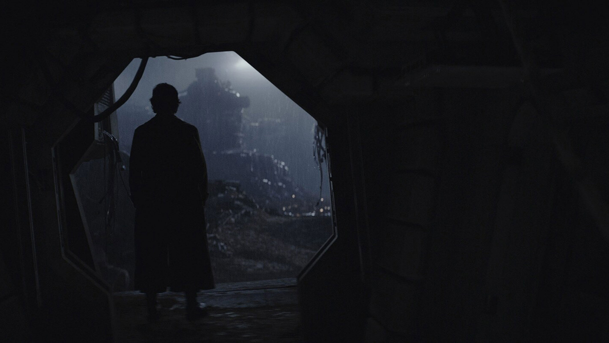 A silhouette of a man is standing in a dark opening. 