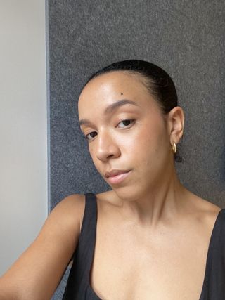 Editor Lauren Tappan stands in front of a blank wall wearing a black tank top and Rhode blush in the shade Freckle