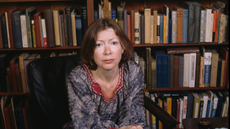 Joan Didion sitting in front of a bookshelf 