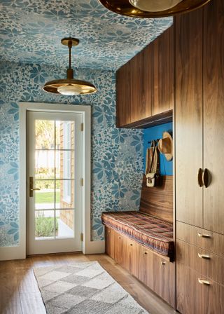 Mudroom entryway with blue floral patterned wallpaper, wood floor, and built-in wooden cabinetry