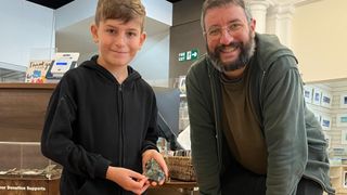 A man and a boy standing together. The boy is holding a Neanderthal axe head.