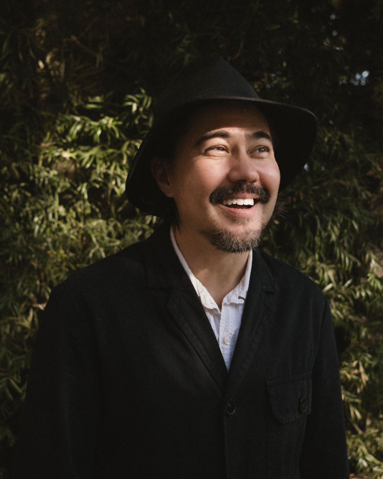 a man with a beard wearing a collared shirt with a black jacket and hat
