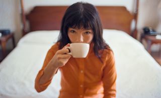 Björk sits on end of hotel bed drinking coffee