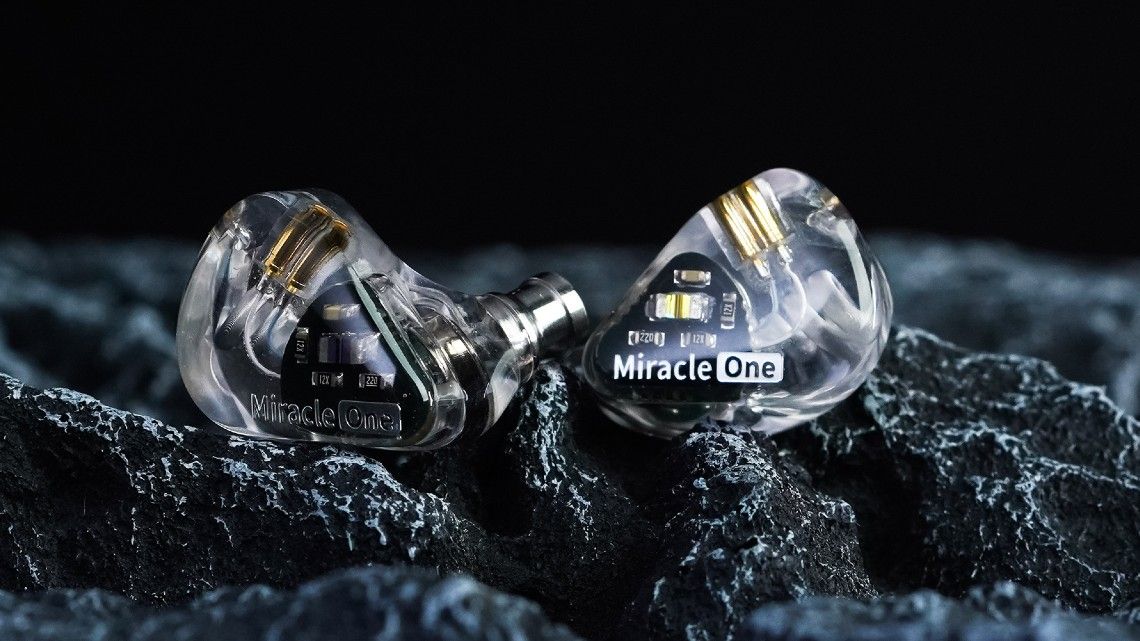 A pair of transparent Aful MiracleOne earbuds rests on dark textured rock