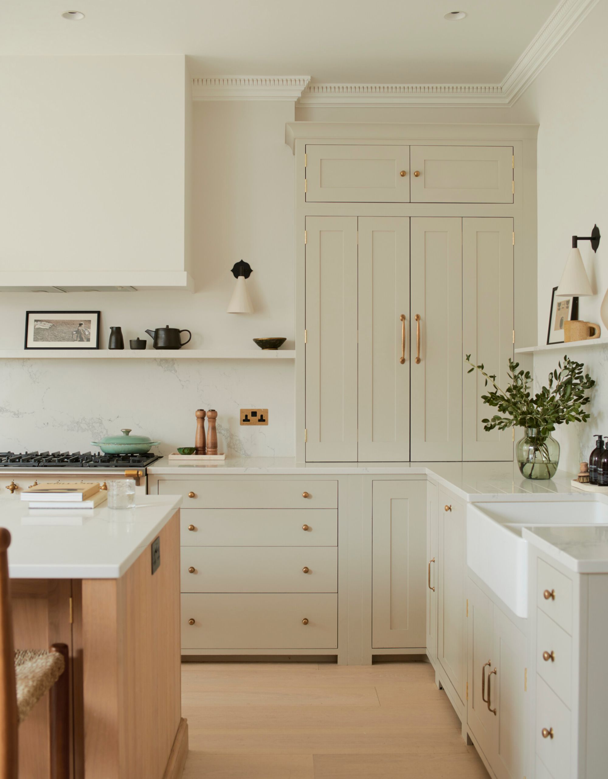 A light off white kitchen with high ceiling and architectural moldings, a kitchen island and a boxed in custom extractor above the cooker