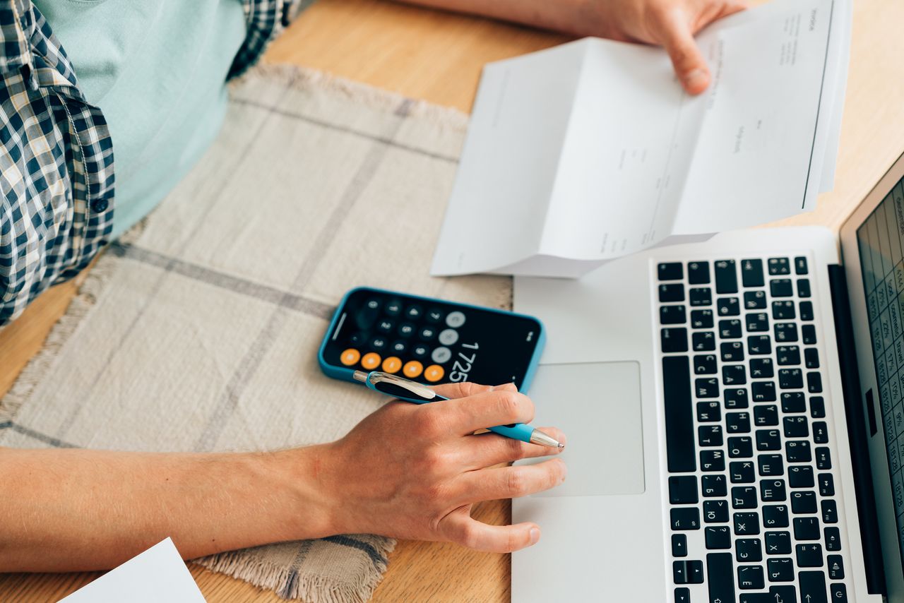 Person managing their personal finances, looking at a bill, a calculator and a laptop.