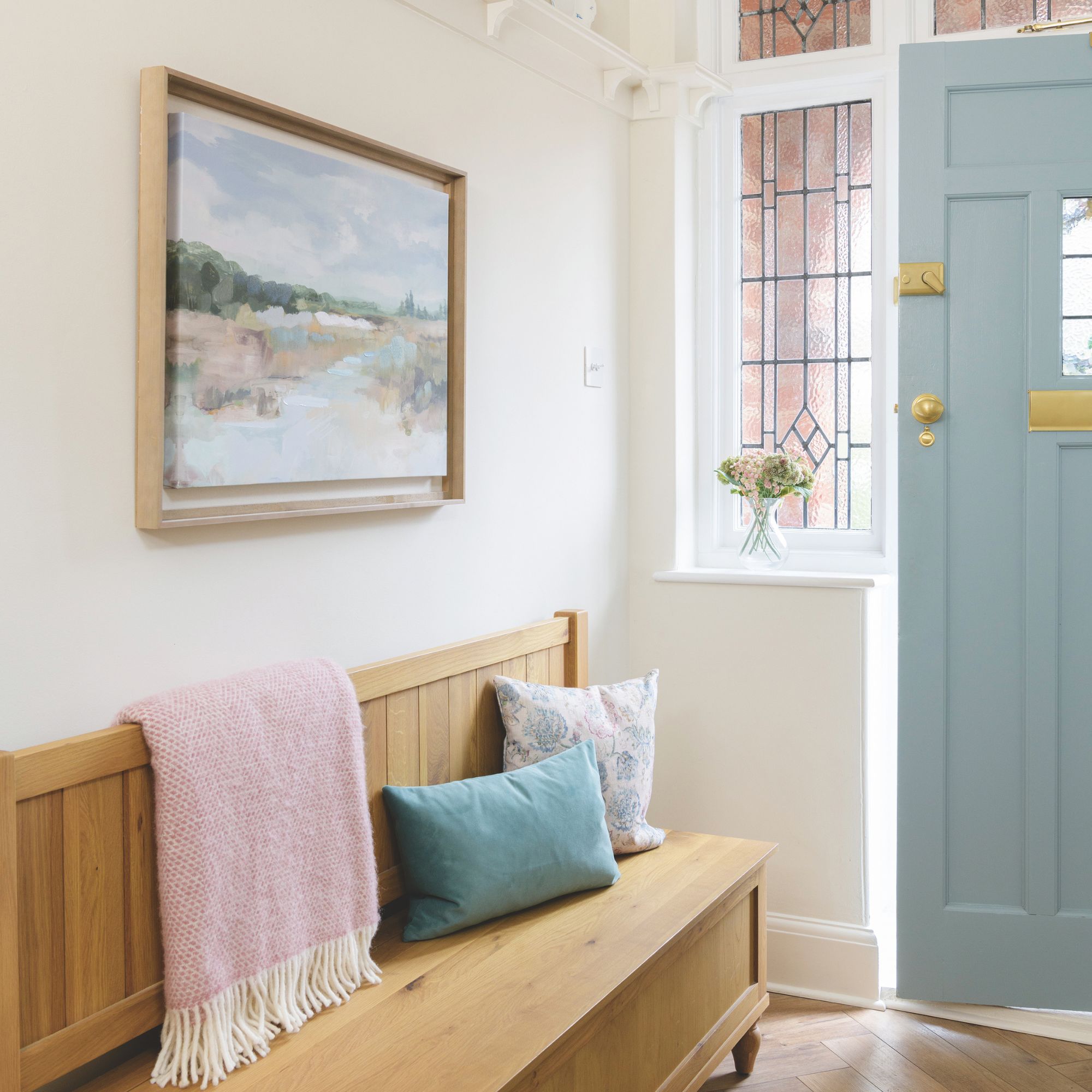 White painted hallway with a blue front door and a wooden storage bench with cushions and a blanket on it