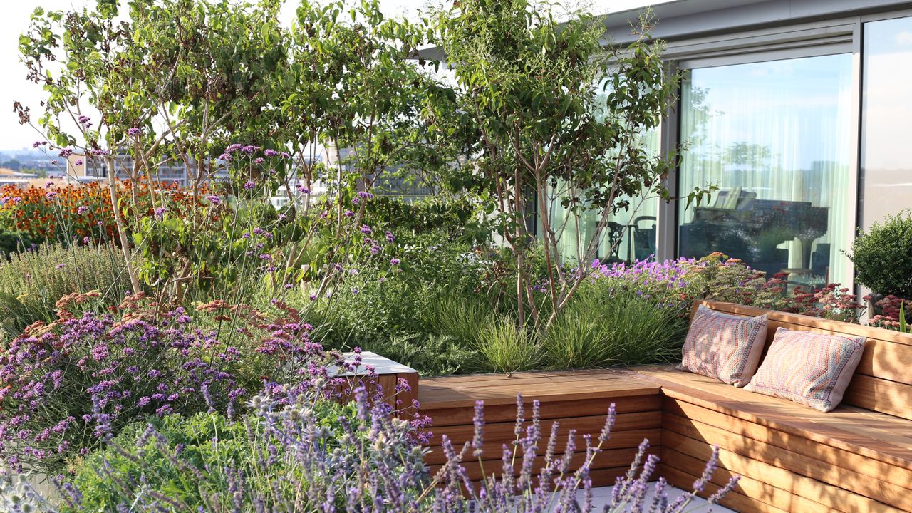 An example of roof garden ideas showing meadow style planting and a built-in L shaped wooden bench seating.