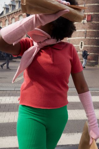 A woman wearing a pink scarf, pink elbow high gloves, a pink short sleeve shirt and green striped pants.