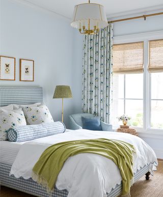 Bedroom with pale blue walls, bed dressed in white and blue and window dressed with shade and drapes