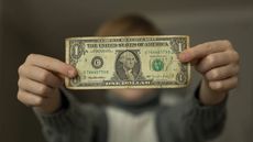Boy holds a battered one dollar bill in front of him.