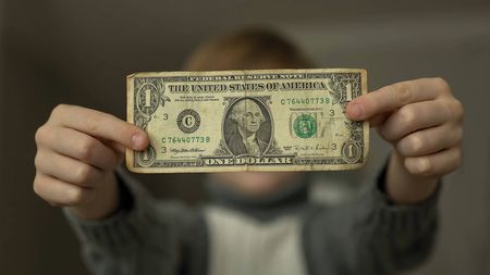 Boy holds a battered one dollar bill in front of him.
