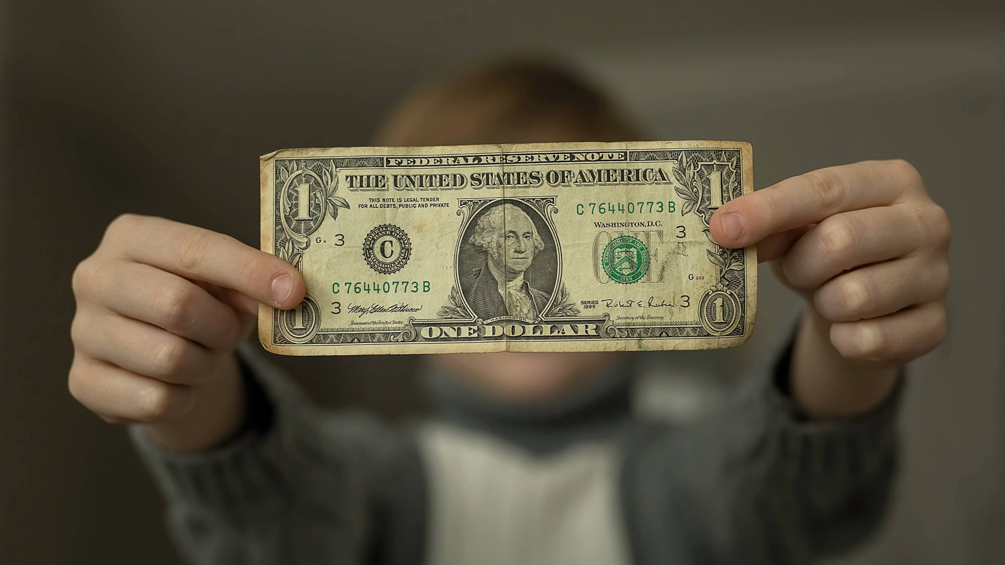 Boy holds a battered one dollar bill in front of him.
