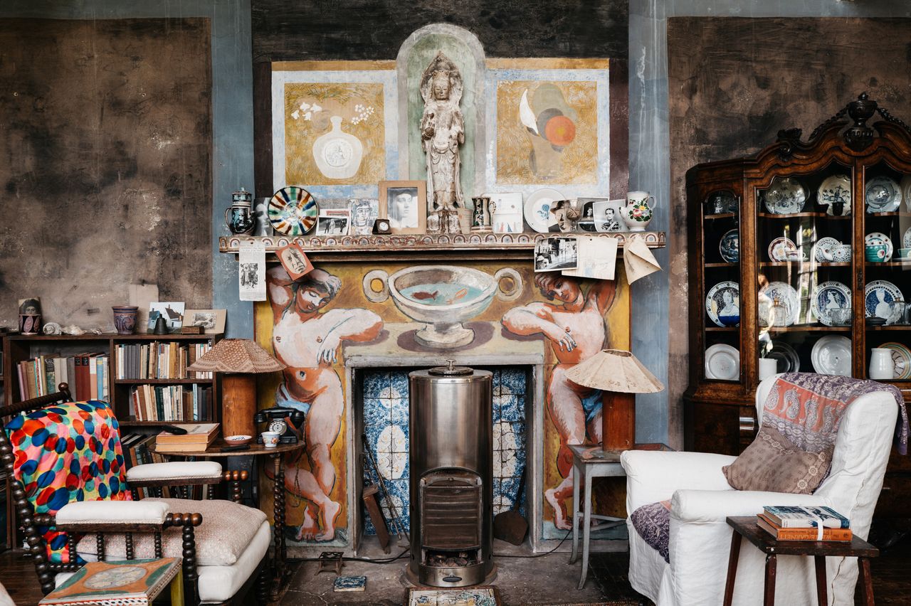A richly ornate artist studio is filled with yellowed books, furniture, postcards, ephemera, and china porcelain kept in an antique cupboard and decorated with handpainted figurative murals.