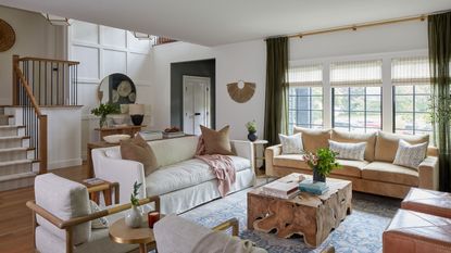 living room with stairs white sofas rough cut tree trunk coffee table patterned rug leather footstools with steel framed windows