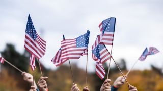 A crowd of hands waving US flags outside