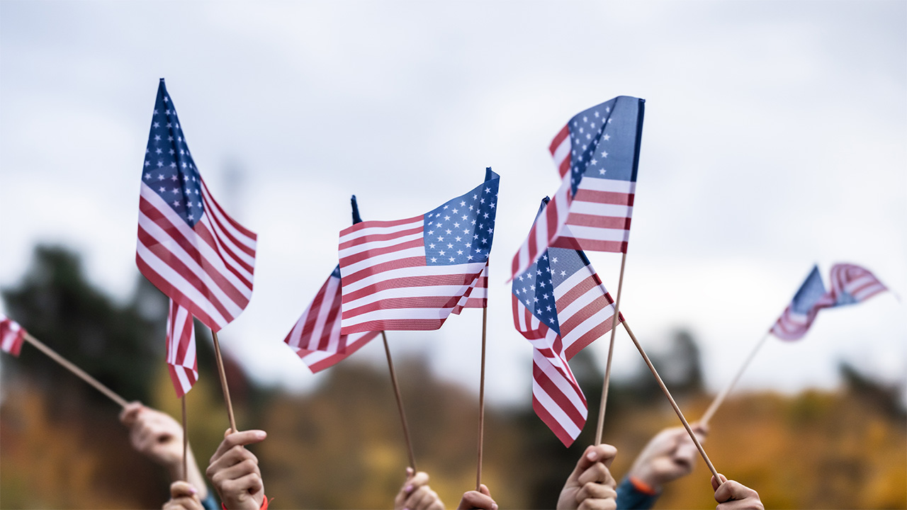 A crowd of hands waving US flags outside